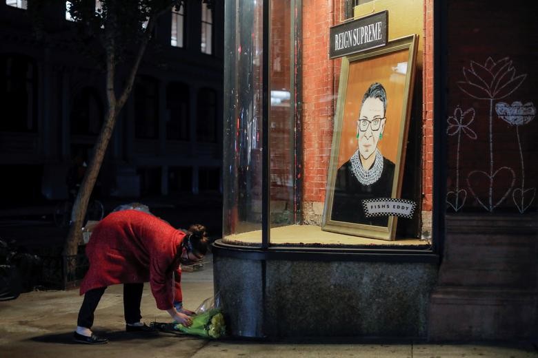A person places flowers in front of a painting in a storefront on Broadway of Associate Justice of the Supreme Court of the United States Ruth Bader Ginsburg who passed away in Manhattan, New York City, September 18, 2020. REUTERS/Andrew Kelly